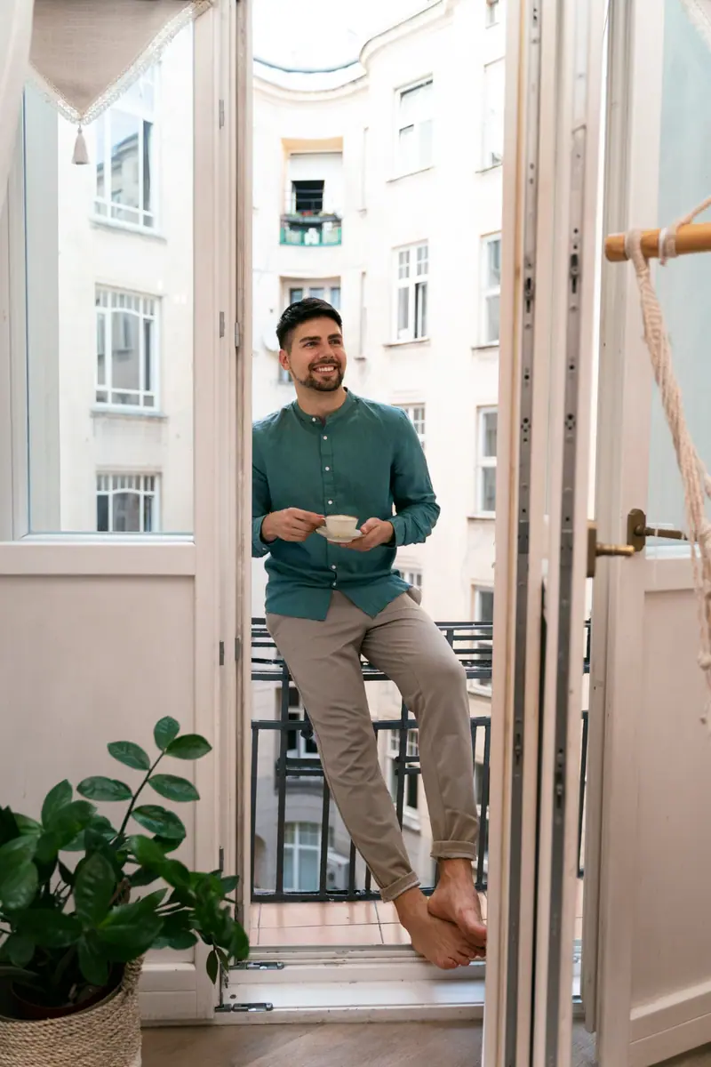 Senhorio à janela de um apartamento, com uma chávena na mão