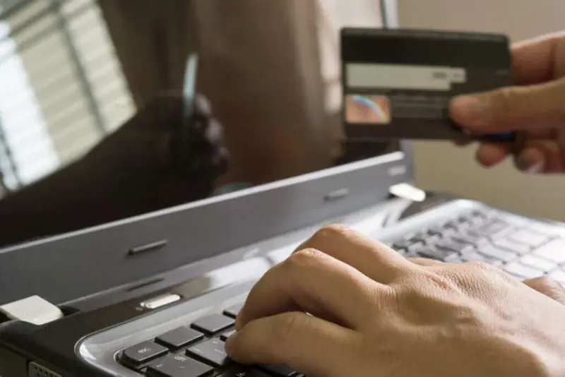 Hand holding a card next to a laptop, illustrating automatic rent collection